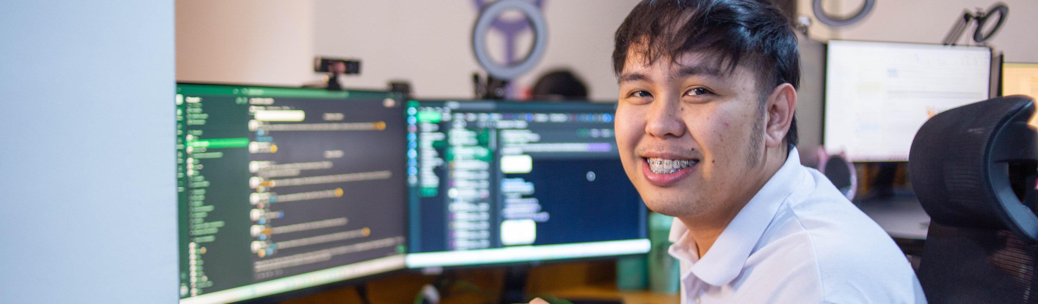 Yoonet teammate smiling at his desk with dual monitors in our Balanga office