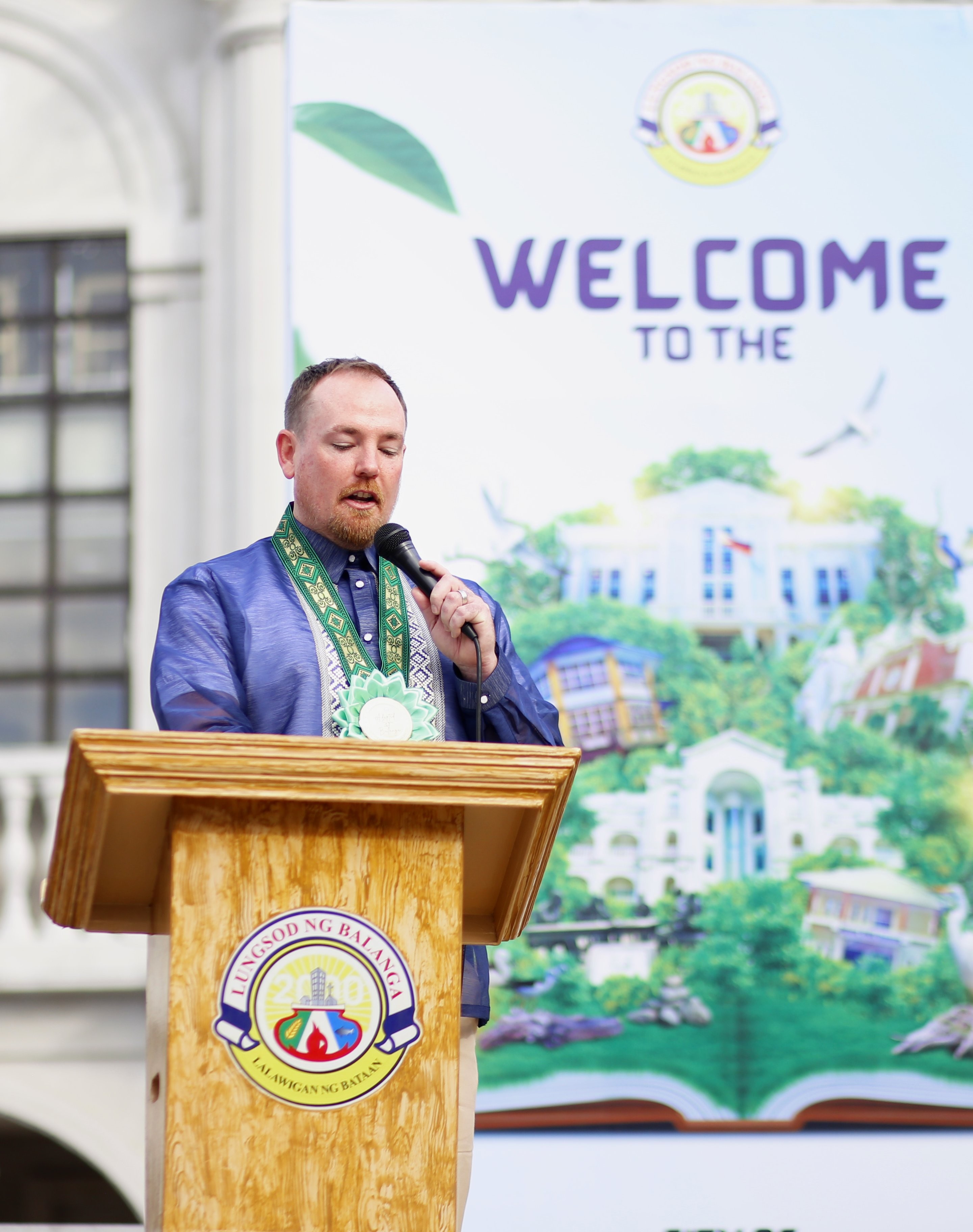Yoonet founder Ben Carter speaking at the Balanga City podium beside a welcome banner for the city