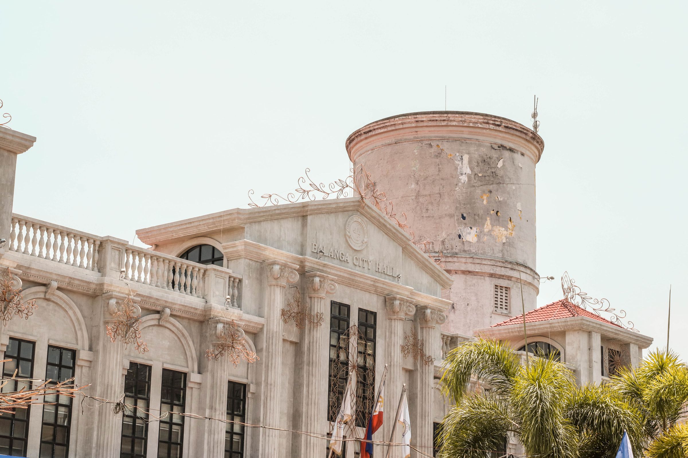 The colonial facade of Balanga City Hall with palm trees against a clear sky