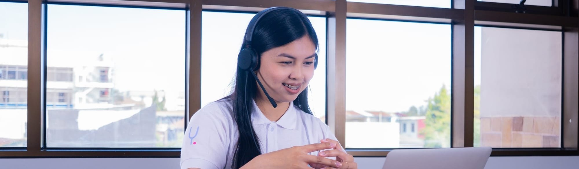 A Yoonet virtual medical receptionist wearing a headset on a video call at her laptop in the Balanga office