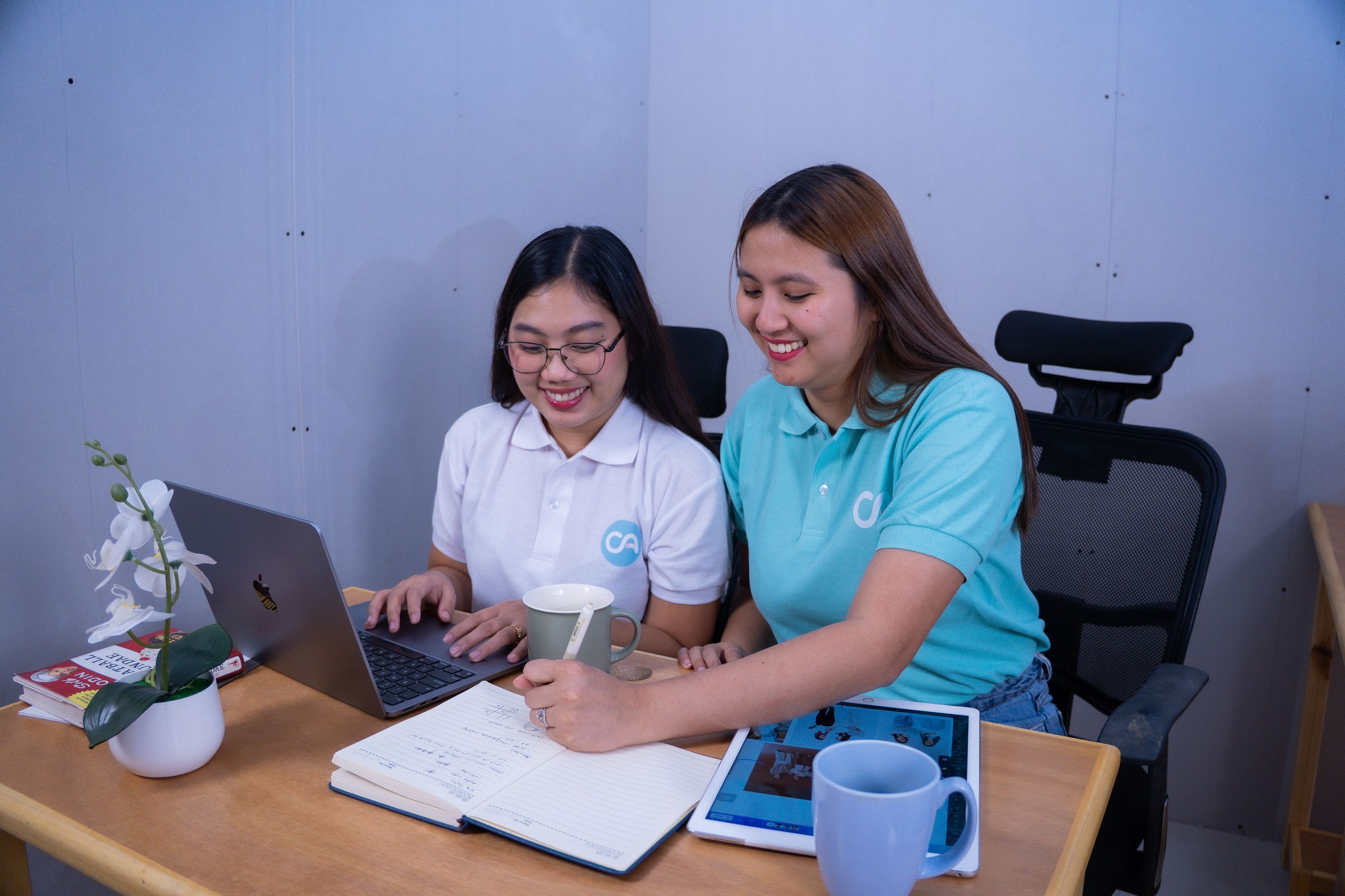 Two Clinic Admin teammates in matching polos reviewing patient notes together at a laptop