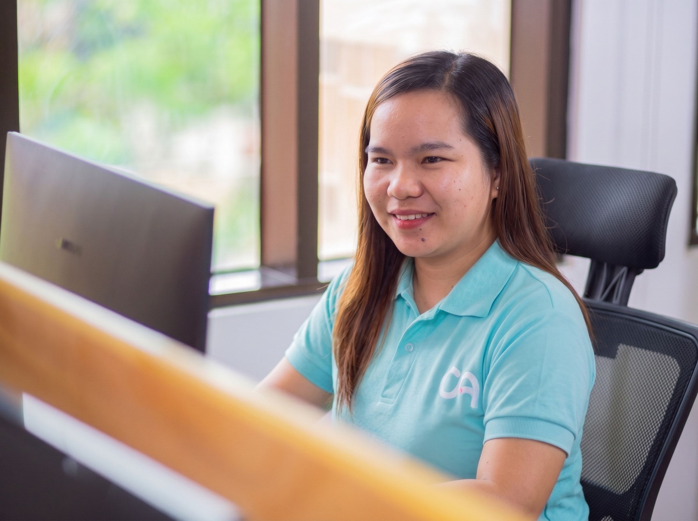 Yoonet practice admin teammate wearing a Clinic Admin polo, smiling at her desk in front of dual monitors